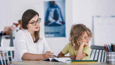 
		A woman sits at the table with a child and helps with homework.
	